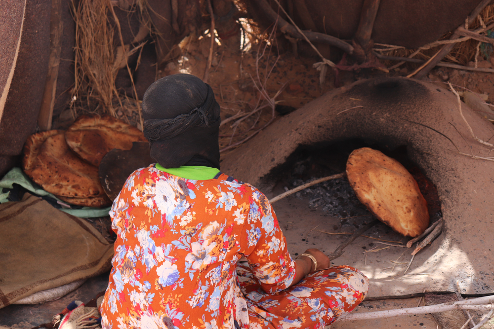 Donna marocchina che cuoce il pane sotto sabbia